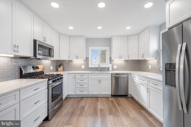 kitchen with sink, tasteful backsplash, light hardwood / wood-style flooring, white cabinets, and appliances with stainless steel finishes