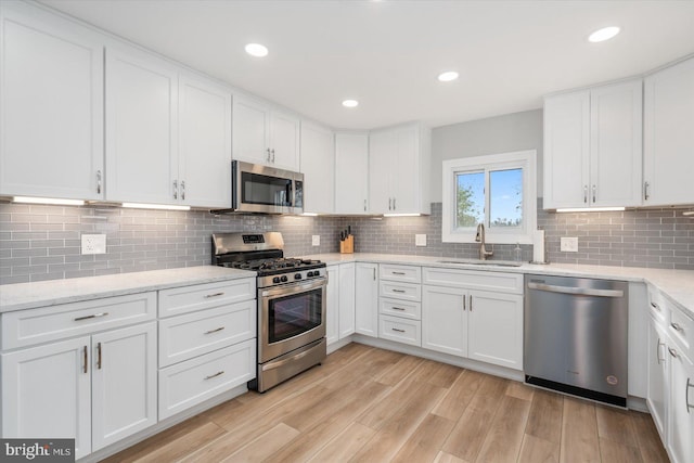 kitchen featuring sink, light wood-type flooring, tasteful backsplash, white cabinetry, and stainless steel appliances