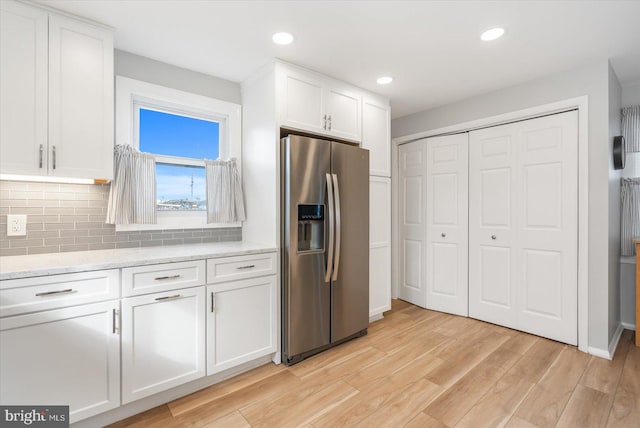 kitchen featuring light stone countertops, stainless steel refrigerator with ice dispenser, light hardwood / wood-style floors, decorative backsplash, and white cabinets