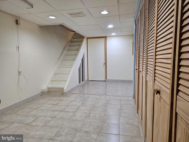 basement with a paneled ceiling and light tile patterned flooring