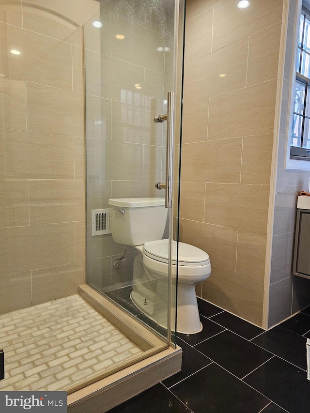 bathroom featuring tile patterned flooring, toilet, tile walls, and walk in shower