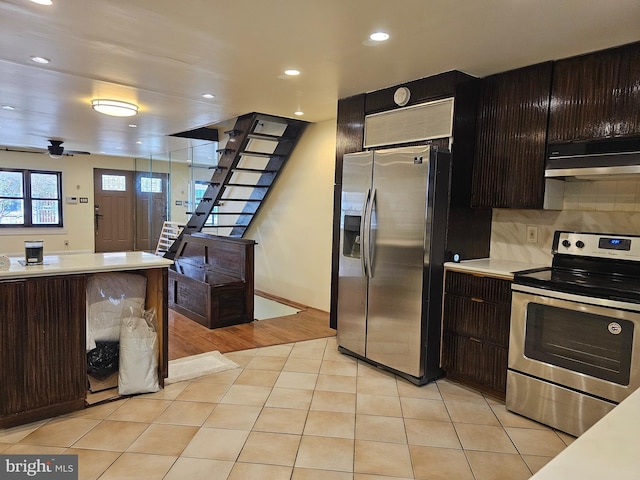 kitchen with ventilation hood, dark brown cabinetry, stainless steel appliances, and light tile patterned flooring