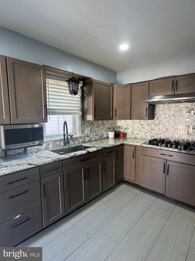 kitchen with black gas stovetop, sink, tasteful backsplash, dark brown cabinets, and light stone counters