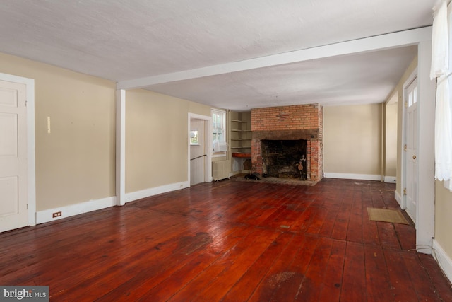 unfurnished living room with a brick fireplace, built in shelves, radiator, and hardwood / wood-style flooring