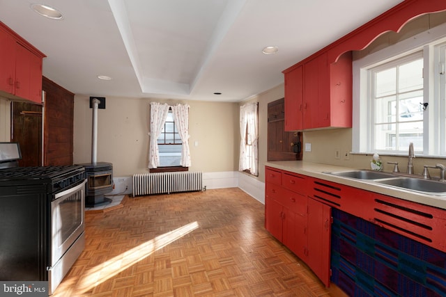 kitchen with stainless steel gas range oven, a wood stove, sink, radiator heating unit, and light parquet flooring