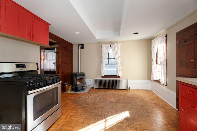 kitchen featuring ornamental molding, gas range, radiator heating unit, light parquet flooring, and a wood stove