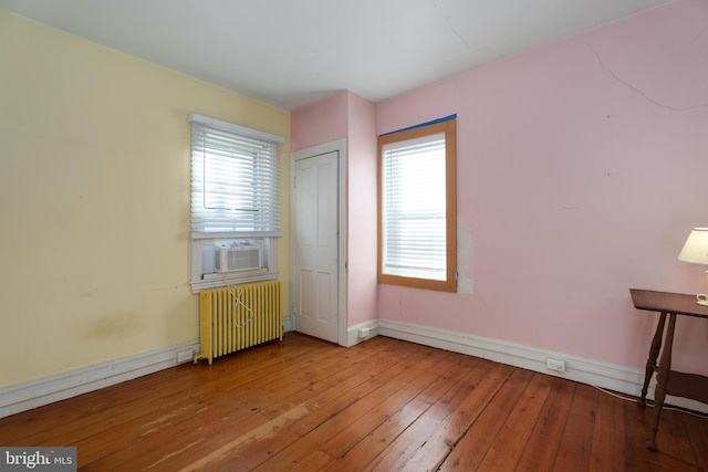 unfurnished bedroom with cooling unit, light hardwood / wood-style flooring, radiator, and multiple windows