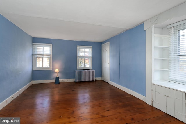 empty room with a wealth of natural light, dark hardwood / wood-style flooring, and radiator