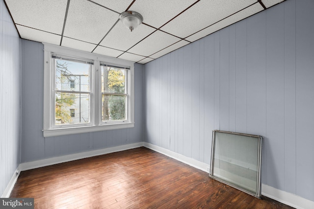 unfurnished room featuring a drop ceiling, wood walls, and dark wood-type flooring