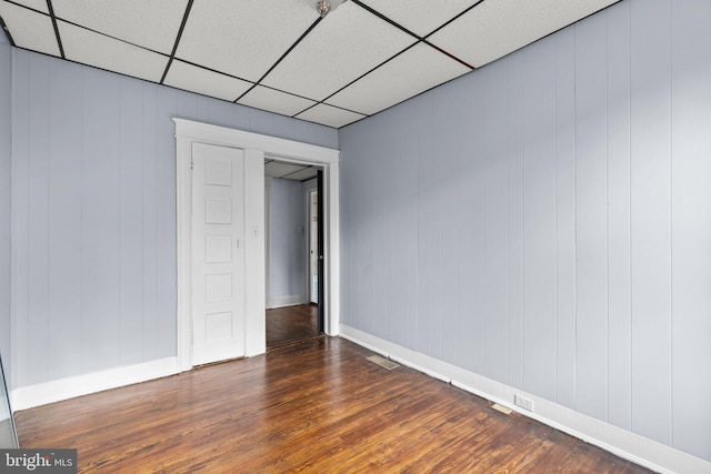 empty room featuring a paneled ceiling, wood walls, and dark hardwood / wood-style flooring