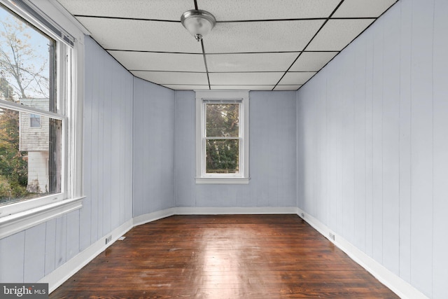 empty room featuring a paneled ceiling, dark wood-type flooring, and wooden walls