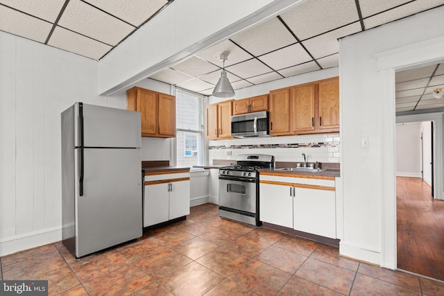 kitchen featuring appliances with stainless steel finishes, tasteful backsplash, a drop ceiling, sink, and pendant lighting