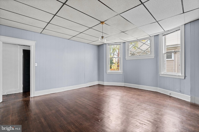 unfurnished room with a drop ceiling, wood walls, and dark hardwood / wood-style flooring