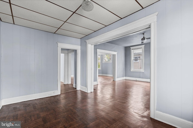 empty room with dark parquet flooring, a drop ceiling, wooden walls, and ceiling fan