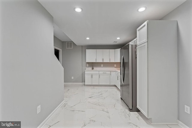 kitchen with white cabinetry, sink, and stainless steel refrigerator