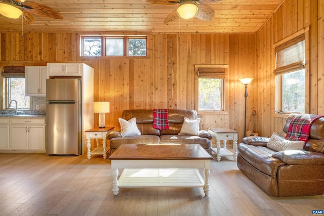 living room with ceiling fan, sink, wooden walls, wood ceiling, and light wood-type flooring