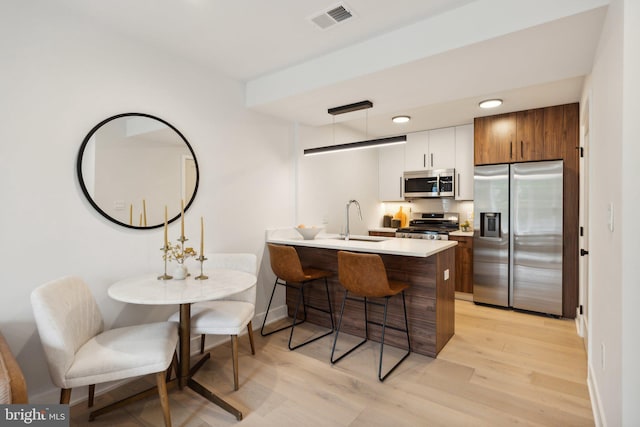 kitchen featuring kitchen peninsula, light wood-type flooring, stainless steel appliances, sink, and white cabinets