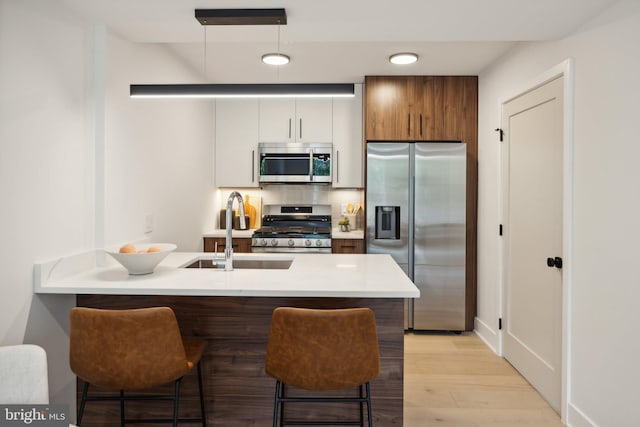 kitchen featuring stainless steel appliances, sink, light hardwood / wood-style flooring, white cabinets, and a breakfast bar area