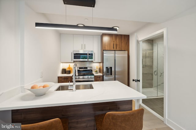 kitchen featuring white cabinetry, sink, stainless steel appliances, kitchen peninsula, and light wood-type flooring