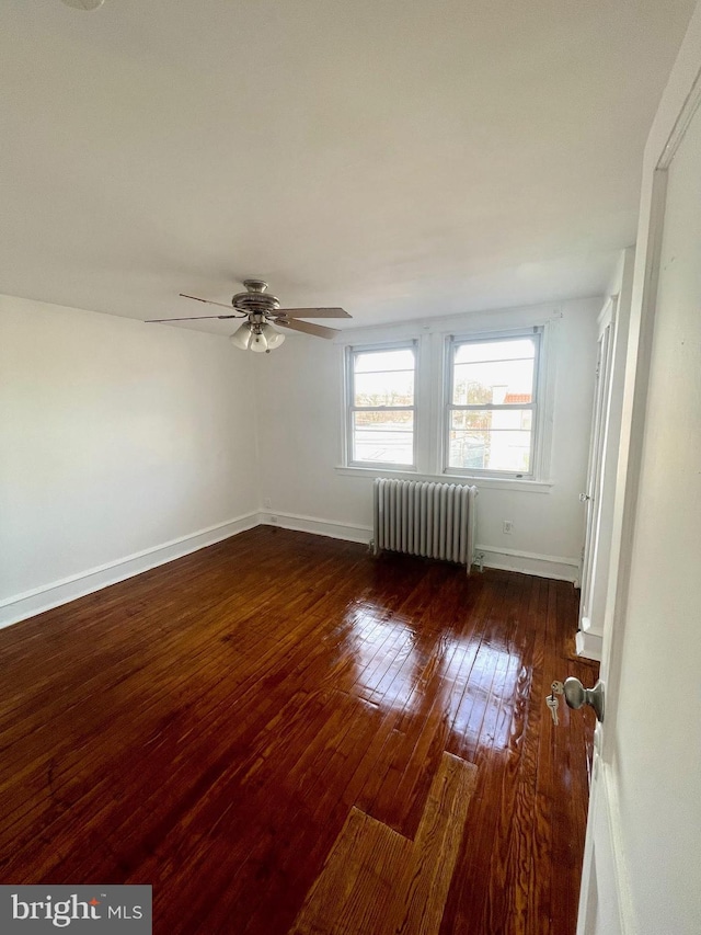 empty room with dark hardwood / wood-style floors, radiator, and ceiling fan