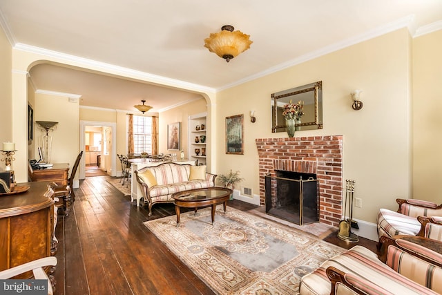 living room featuring built in features, dark hardwood / wood-style flooring, ornamental molding, and a brick fireplace