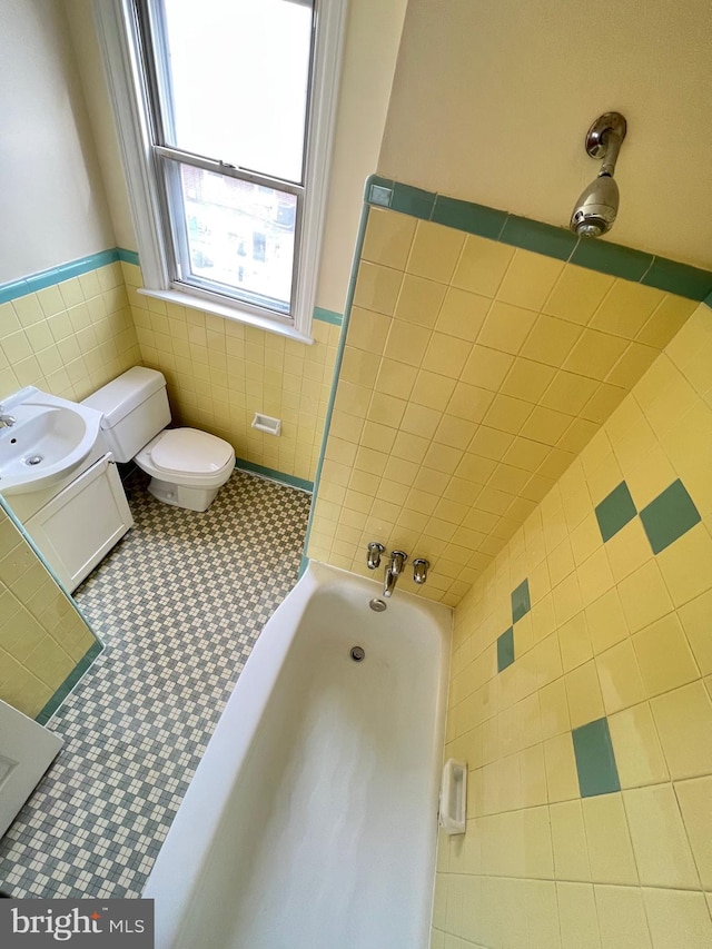 bathroom featuring a bathtub, vanity, tile patterned floors, toilet, and tile walls