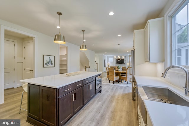 kitchen featuring pendant lighting, a center island, sink, light hardwood / wood-style flooring, and dark brown cabinets