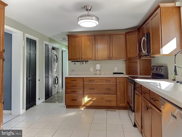 kitchen with sink, light tile patterned floors, stacked washing maching and dryer, and appliances with stainless steel finishes