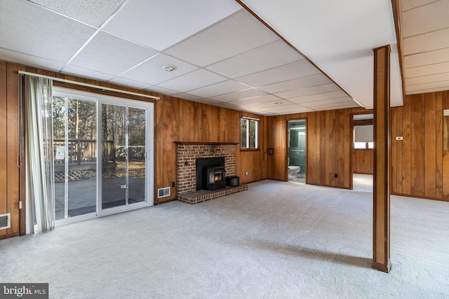 unfurnished living room with a wood stove, wood walls, and light colored carpet