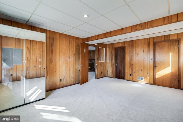 empty room featuring a paneled ceiling, wooden walls, electric panel, and carpet