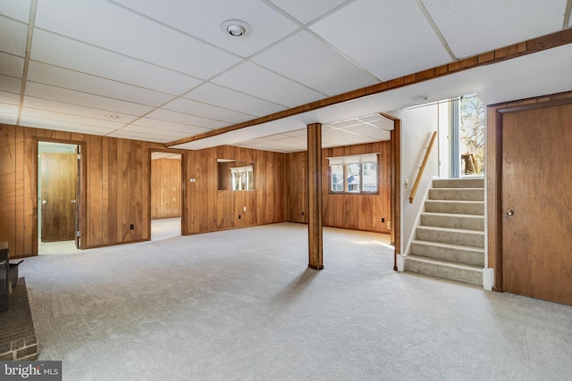 basement with light carpet, a drop ceiling, and wood walls