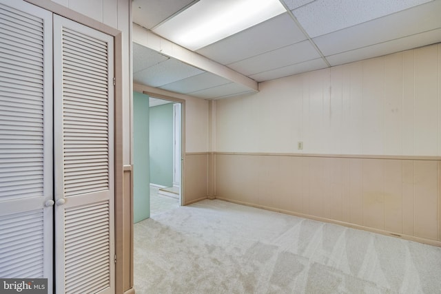 basement featuring a paneled ceiling and light carpet