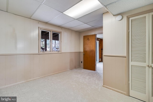 empty room with light carpet, a paneled ceiling, and wooden walls