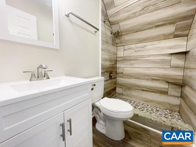 bathroom featuring a tile shower, vanity, wood-type flooring, and toilet