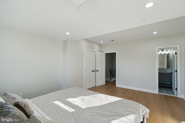 bedroom featuring ensuite bath, a closet, hardwood / wood-style floors, and sink