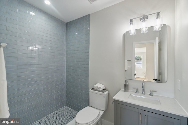 bathroom featuring a tile shower, vanity, and toilet