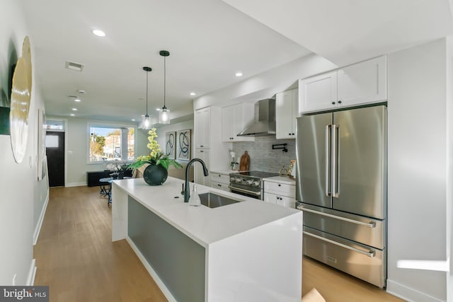 kitchen with white cabinetry, sink, wall chimney exhaust hood, a center island with sink, and appliances with stainless steel finishes