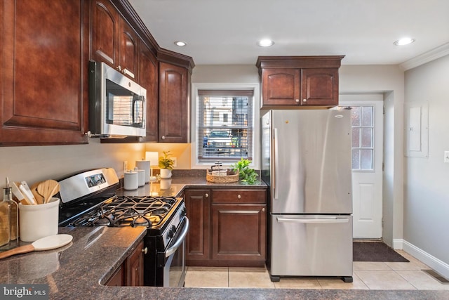 kitchen featuring stainless steel appliances, crown molding, light tile patterned floors, dark stone countertops, and electric panel