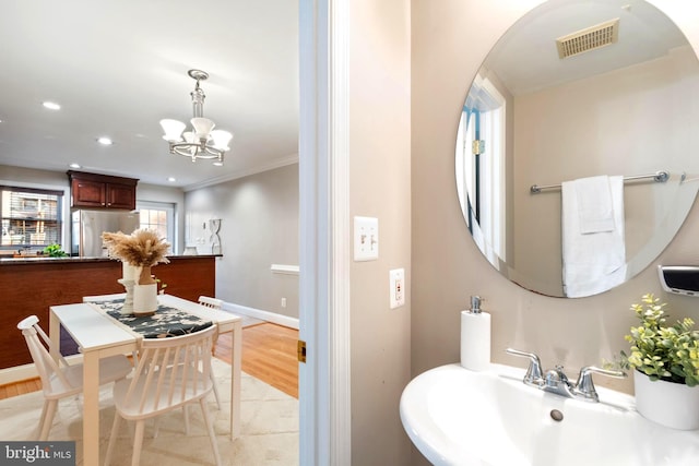 bathroom with hardwood / wood-style flooring, a notable chandelier, crown molding, and sink