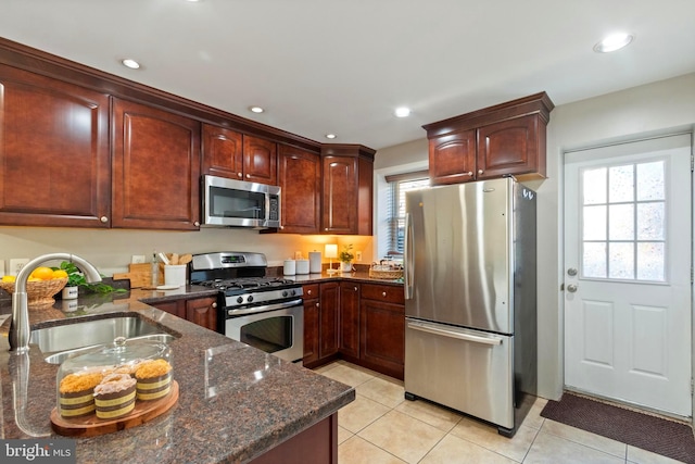 kitchen with dark stone countertops, sink, light tile patterned floors, and stainless steel appliances