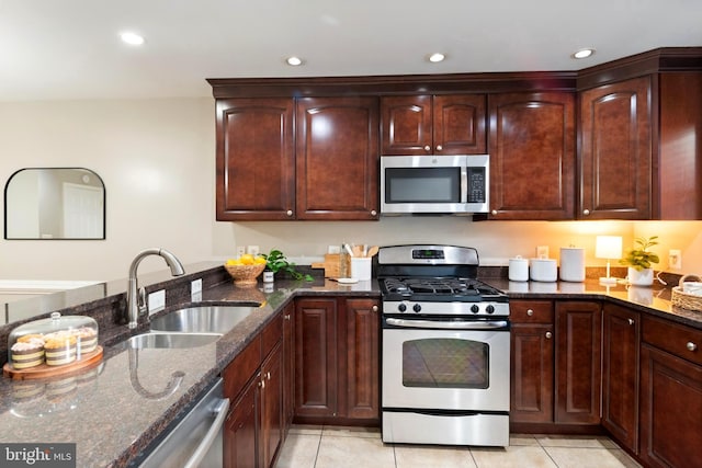 kitchen featuring sink, dark stone countertops, light tile patterned floors, and stainless steel appliances