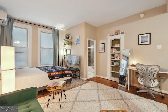 bedroom with baseboards, wood finished floors, and a wall mounted AC