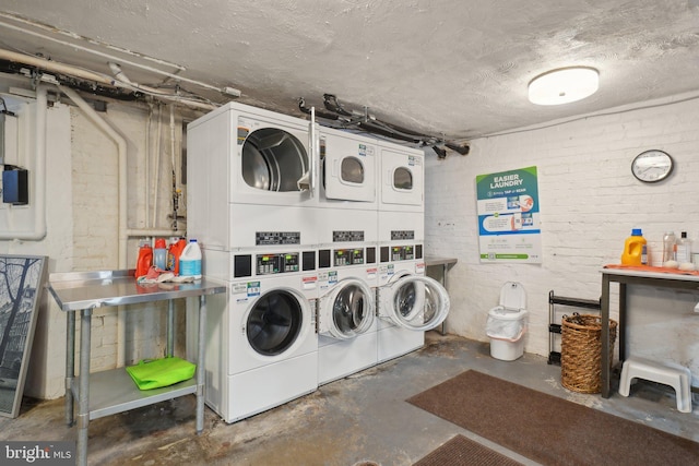 common laundry area featuring stacked washer and dryer, brick wall, a textured ceiling, and washing machine and clothes dryer