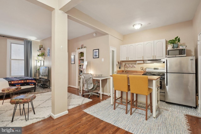 kitchen with light wood finished floors, stainless steel appliances, white cabinets, baseboards, and exhaust hood