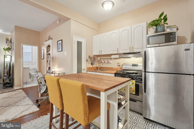 kitchen featuring under cabinet range hood, a sink, wood counters, white cabinets, and appliances with stainless steel finishes