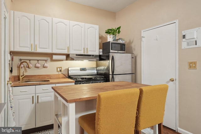 kitchen with white cabinets, wood counters, stainless steel appliances, under cabinet range hood, and a sink