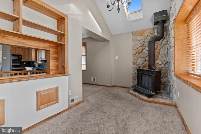 unfurnished living room featuring light carpet, a wood stove, lofted ceiling with skylight, and sink