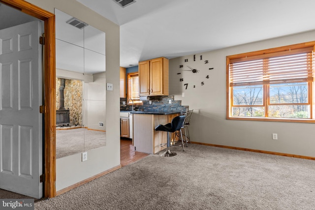 kitchen with a kitchen bar, light brown cabinetry, decorative backsplash, dark carpet, and a wood stove