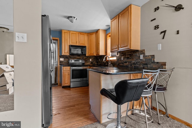 kitchen with a breakfast bar, decorative backsplash, kitchen peninsula, and appliances with stainless steel finishes