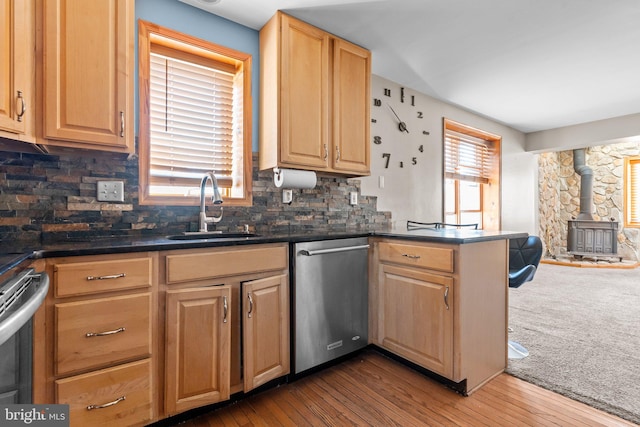 kitchen featuring backsplash, sink, wood-type flooring, dishwasher, and a wood stove